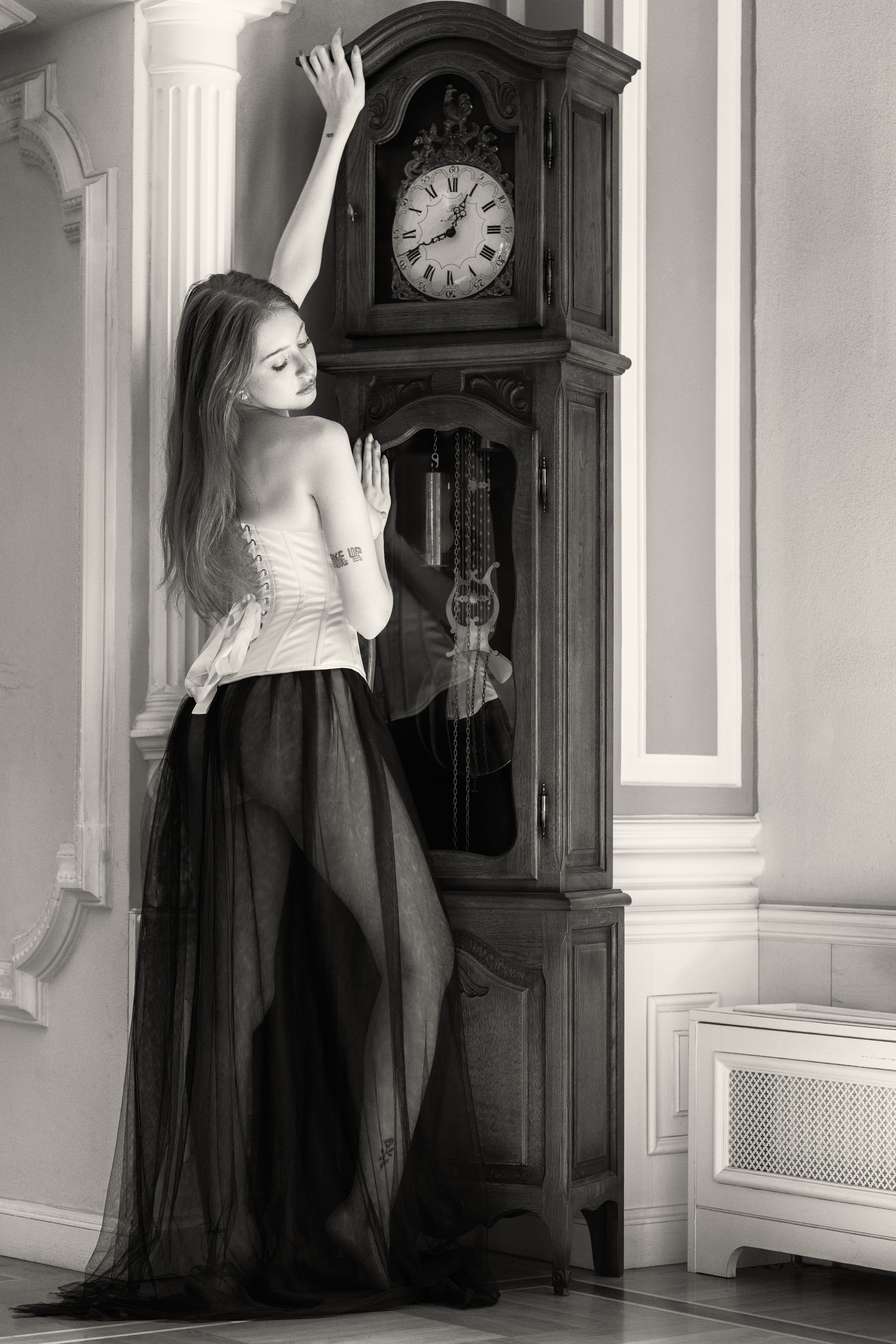 artistic nude, back view, beautiful woman, corset, dark romanticism, elegant pose, feminine grace, grandfather clock, modern muse, monochrome, nostalgic, one person, quiet sensuality, reflection, sheer fabric, standing, vintage aesthetic, young woman, Alex Tsarfin