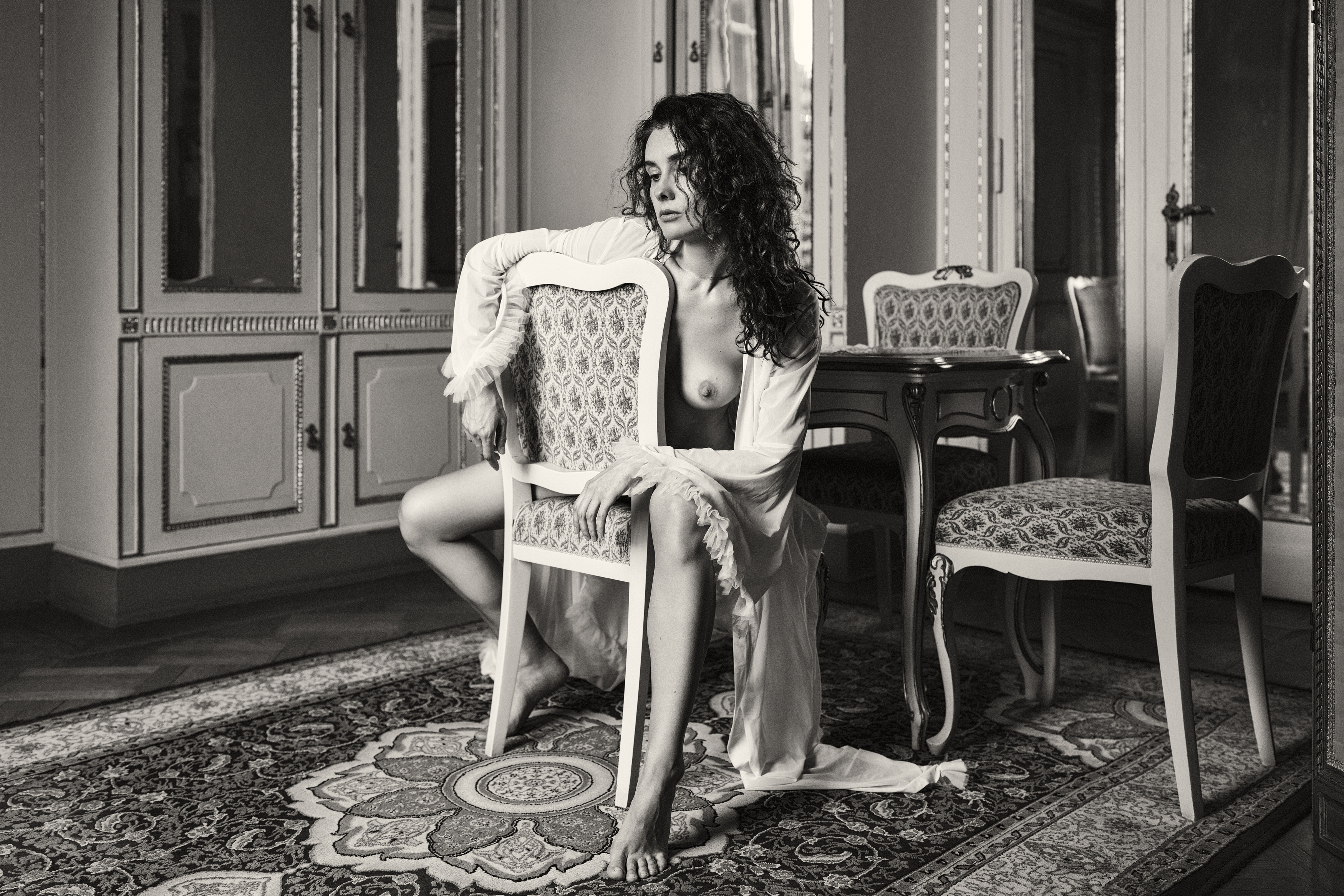 antique interior, artistic nude, chair pose, curly hair, emotional depth, fine art, gilded mirrors, intimate atmosphere, monochrome style, nostalgic tone, ornate furniture, poetic sensuality, romantic nude, sensual silence, vintage aesthetic, woman form, Alex Tsarfin