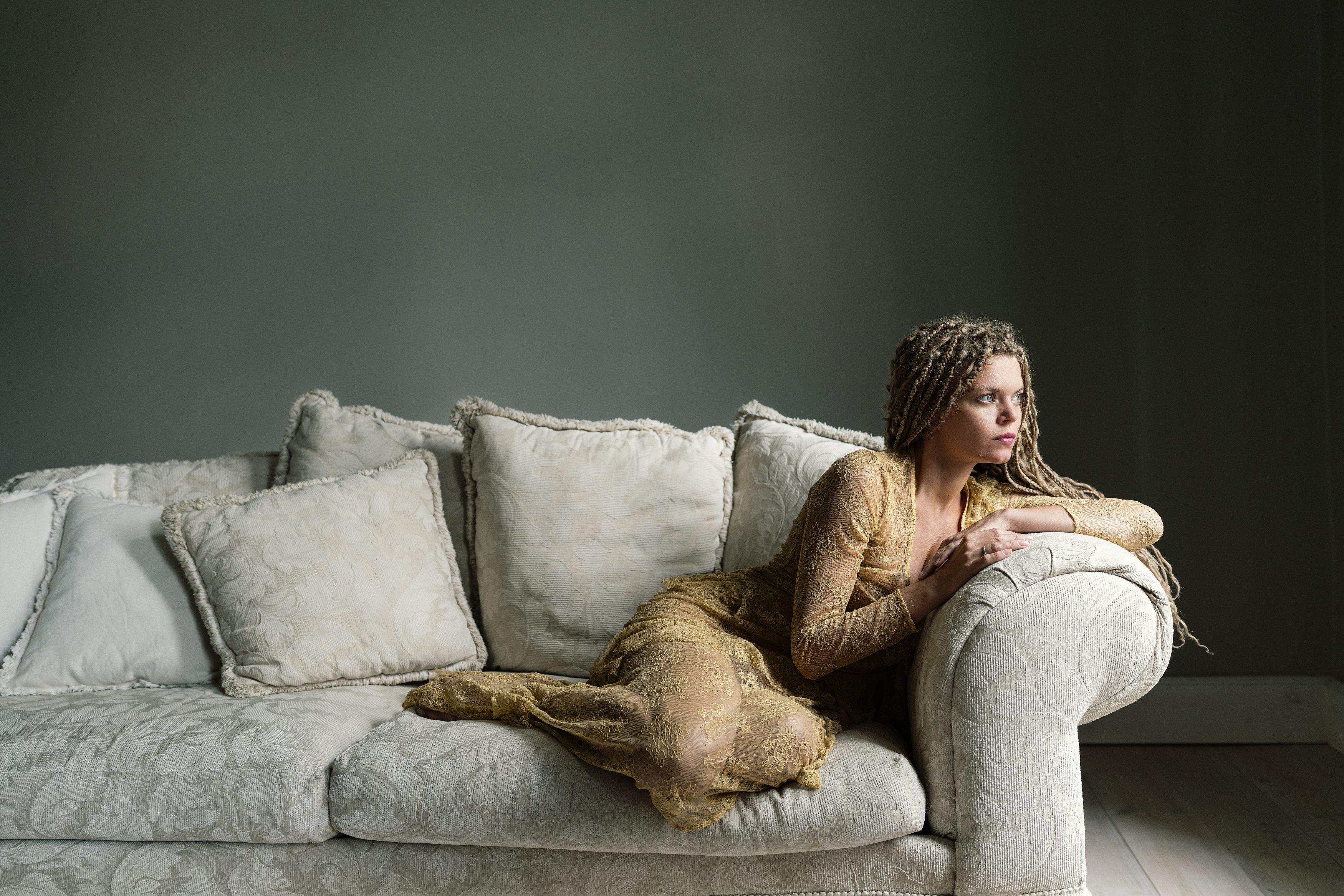 artistic portrait, braided hair, delicate fabric, elegant pose, emotional stillness, golden dress, interior minimalism, introspective gaze, muted palette, neutral décor, restful poise, serene composition, soft light, soft shadows, textured couch, Alex Tsarfin