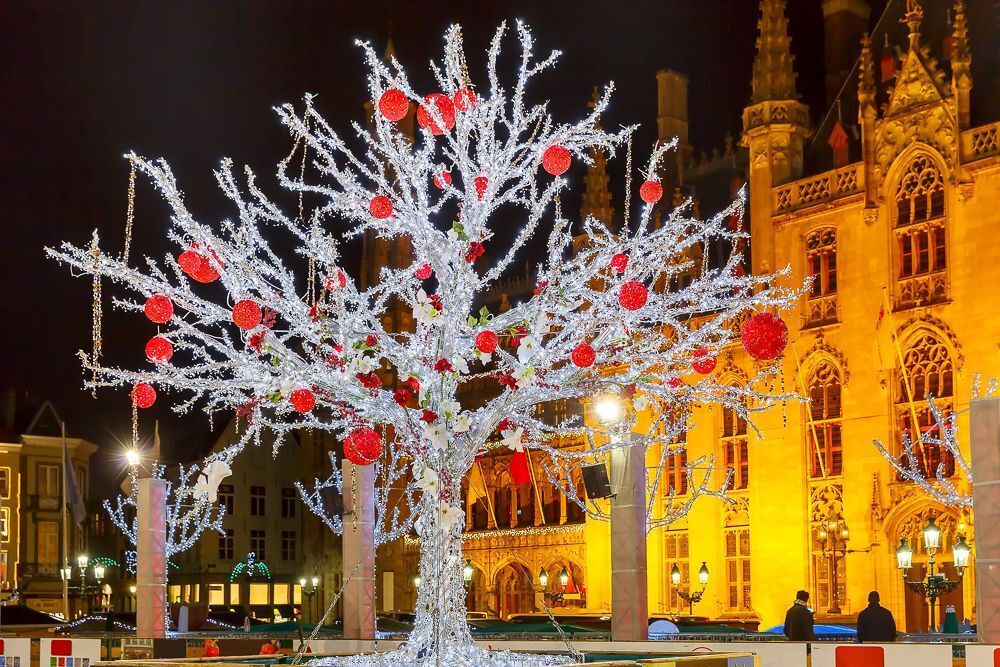 Decorated and illuminated Christmas tree on the rink in front of Province Court at Market Place in the center of Bruges at night, Belgium